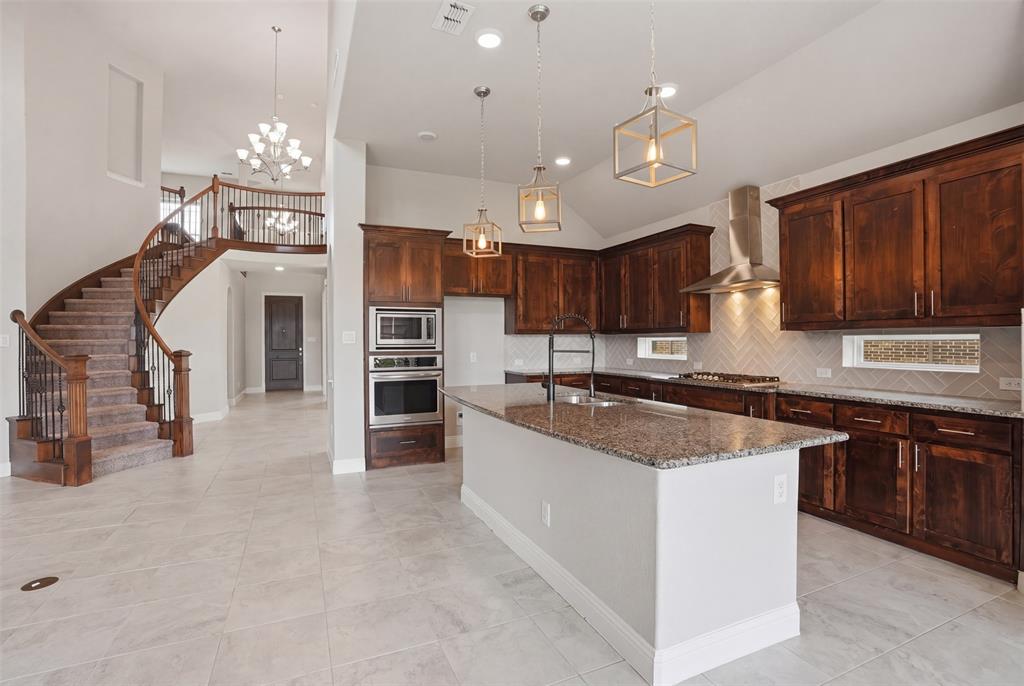 2217 Riviera Drive Little Elm, TX 75068 - Photo 10 of 36 Spacious open-concept interior featuring a grand curved staircase with wrought iron balusters, a gourmet kitchen with dark wood cabinetry, stainless steel appliances including a built-in oven and microwave, a large kitchen island with a stone countertop, and light-toned tile flooring throughout