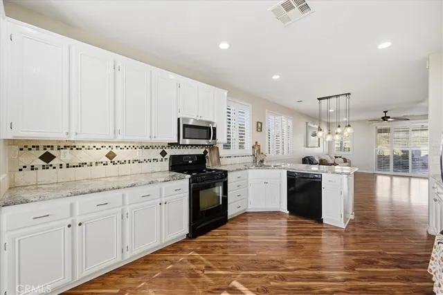 a large white kitchen with stainless steel appliances granite countertop a stove a sink dishwasher and white cabinets with wooden floor