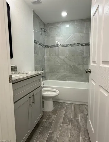 a bathroom with a granite countertop bathtub shower sink vanity and toilet