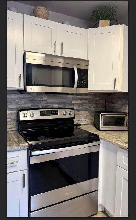 8110 Skillman Street, Unit 2057 Dallas, TX 75231 - Photo 13 of 16 Kitchen with appliances with stainless steel finishes, tasteful backsplash, white cabinets, and light stone countertops