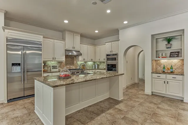 a kitchen with stainless steel appliances granite countertop a refrigerator a sink dishwasher a stove and white cabinets with wooden floor