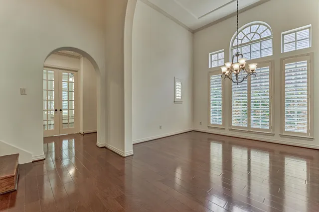 an empty room with wooden floor chandelier and windows