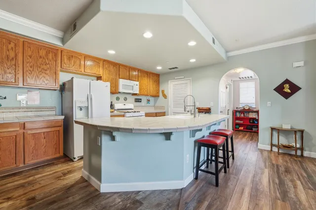 a kitchen with stainless steel appliances granite countertop a refrigerator a sink dishwasher a stove and white countertops with wooden floor