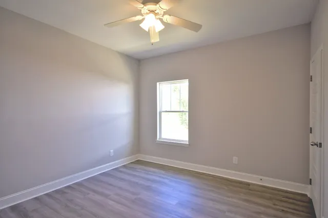 an empty room with wooden floor chandelier fan and windows