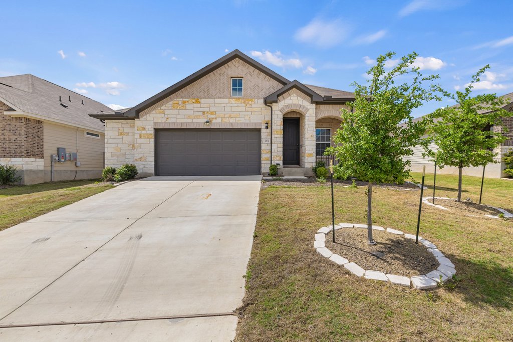 French country home with stone siding, driveway, a front lawn, and a garage
