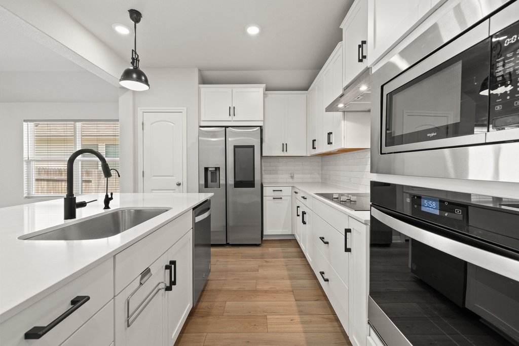 105 Cupa Monti Road Hutto, TX 78634 - Photo 6 of 28 Kitchen with stainless steel appliances, white cabinets, decorative light fixtures, light wood-style floors, and backsplash