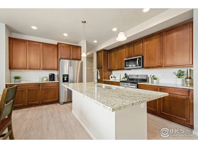 a kitchen with kitchen island granite countertop wooden cabinets a sink dishwasher stove and refrigerator with wooden floor