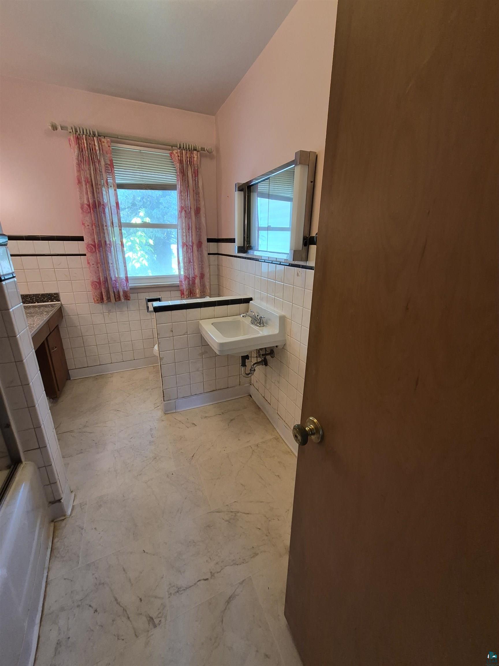 2109 West 22nd Street Duluth, MN 55811 - Photo 13 of 29 Bathroom featuring a wall-mounted sink, a window with blinds, and tiled walls with a black accent border