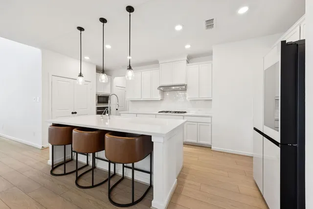 a kitchen with stainless steel appliances granite countertop a sink a stove a refrigerator and island with wooden floor