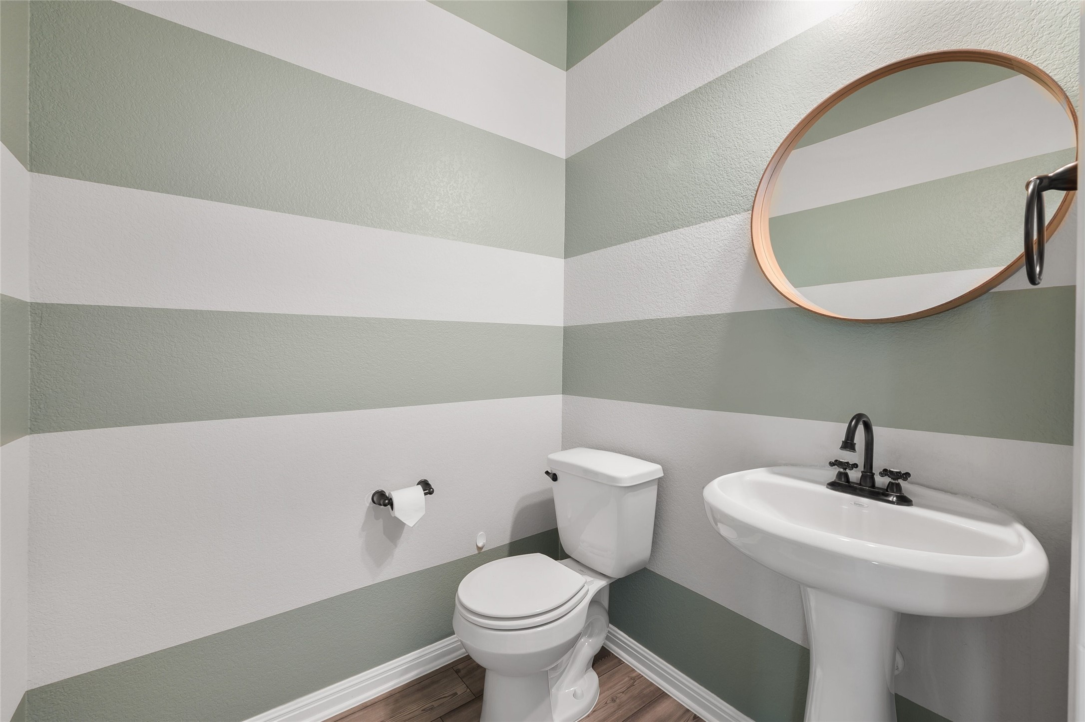 101 Lambert Street Leander, TX 78641 - Photo 27 of 33 Bold striped walls frame this compact powder room, featuring a sleek pedestal sink and wood-look flooring.
