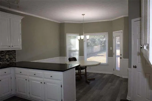 a kitchen with granite countertop white cabinets a sink dishwasher a dining table and chairs with wooden floor