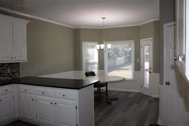 a kitchen with granite countertop white cabinets a sink dishwasher a dining table and chairs with wooden floor