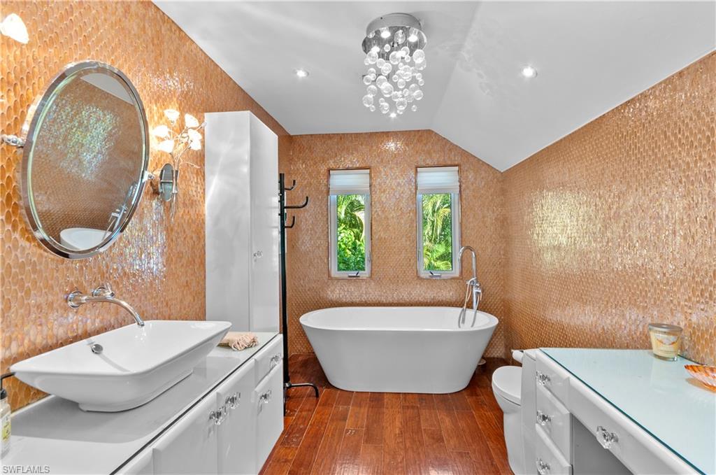 1313 Solana Road, Unit A3 Naples, FL 34103 - Photo 23 of 29 en-suite Bathroom with vanity, vaulted ceiling, dark wood-style flooring, a freestanding tub, and a chandelier