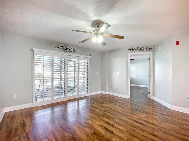 a view of an empty room and kitchen with wooden floor
