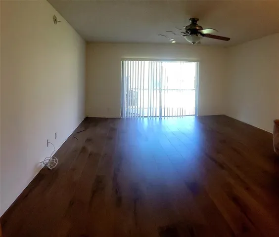 an empty room with wooden floor fan and windows