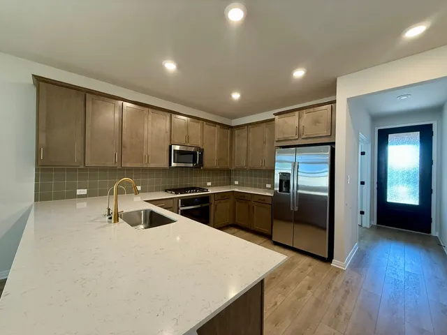 a kitchen with stainless steel appliances a sink a stove top oven a refrigerator with wooden floors