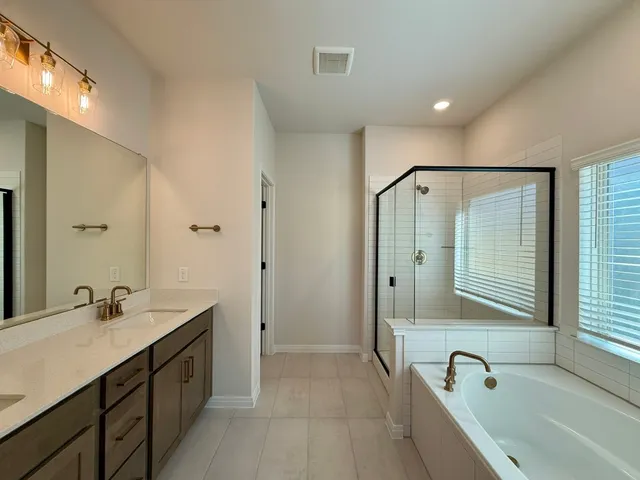 a bathroom with a tub a sink double vanity and a large mirror