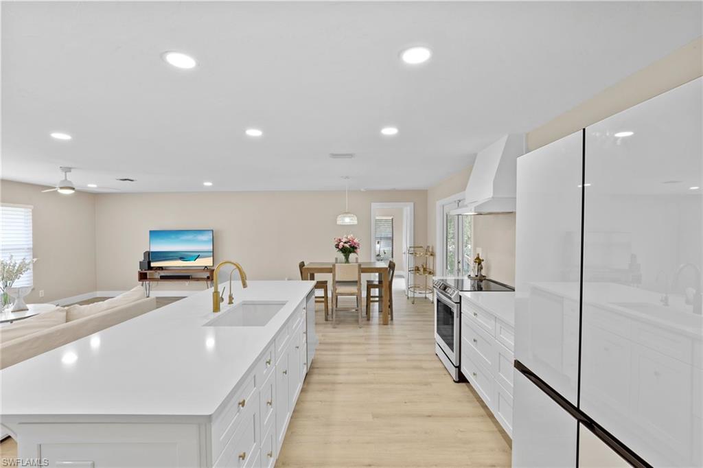 3221 68th Street Southwest Naples, FL 34105 - Photo 8 of 38 a large kitchen with stainless steel appliances a large counter top a sink a stove a refrigerator with white cabinets and wooden floor