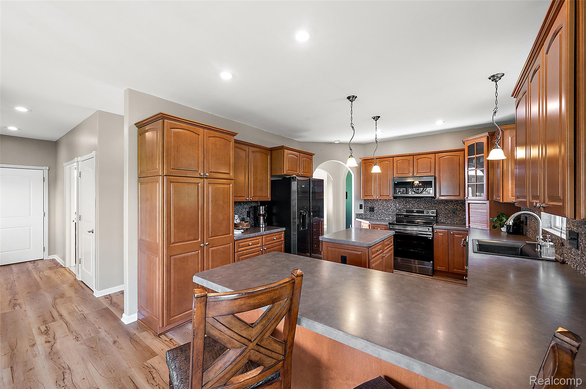 5035 Hidden Ridge Road Metamora, MI 48455 - Photo 23 of 65 Kitchen featuring wood-finish flooring, warm-toned cabinetry, a mosaic tile backsplash, black appliances, and a central island with pendant lighting