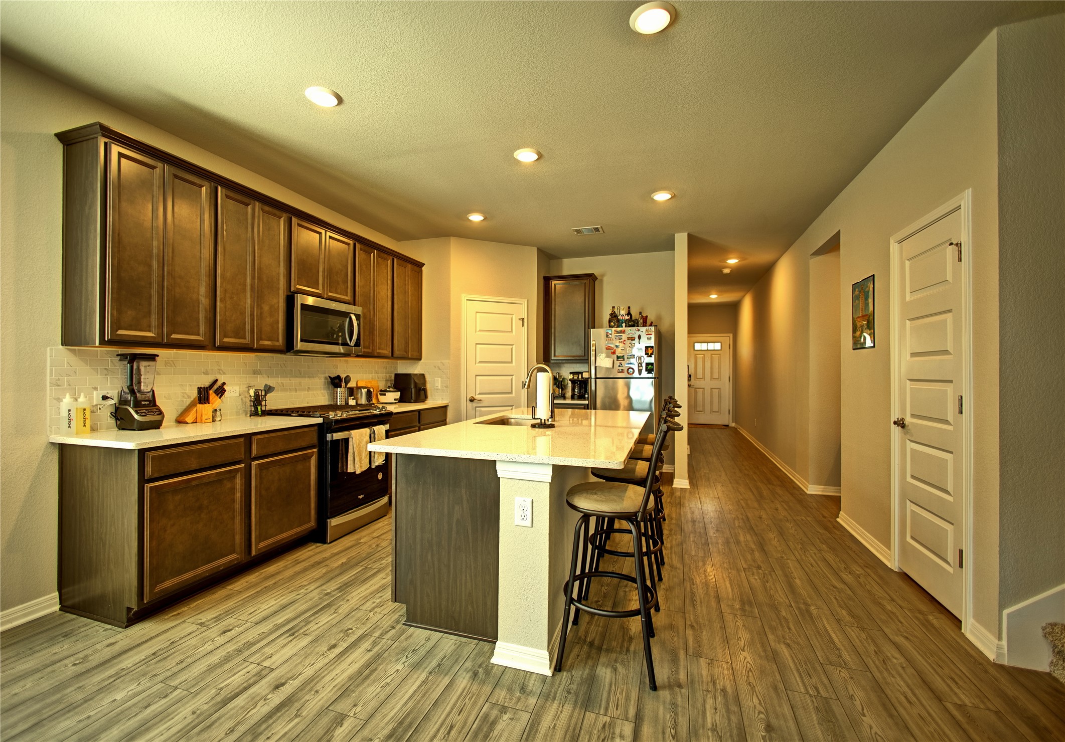 2809 Moyer Lane Round Rock, TX 78665 - Photo 2 of 22 Kitchen featuring stainless steel appliances, dark wood finish cabinets, a kitchen island with sink, light stone counters, and a kitchen breakfast bar