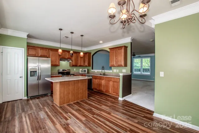 a kitchen with stainless steel appliances granite countertop a refrigerator a sink dishwasher a oven and a dining table with wooden floor