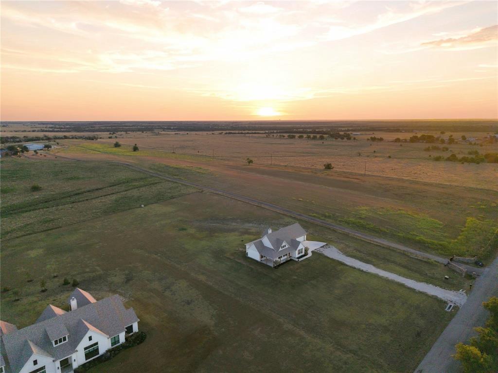 10828 Gregory Road Sanger, TX 76266 - Photo 36 of 37 Expansive rural property featuring a white exterior residence with a gray shingle roof, a gravel driveway, and a large natural pond