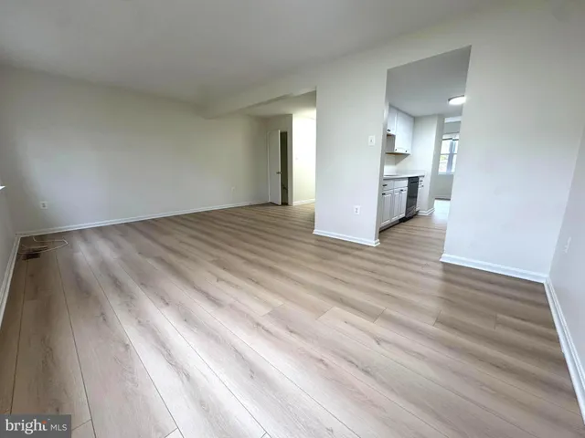 a view of empty room with wooden floor and kitchen