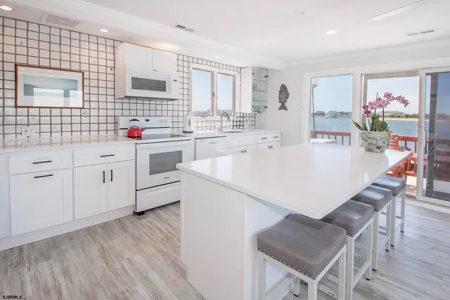 a large white kitchen with stainless steel appliances granite countertop a stove a refrigerator a dining table and chairs