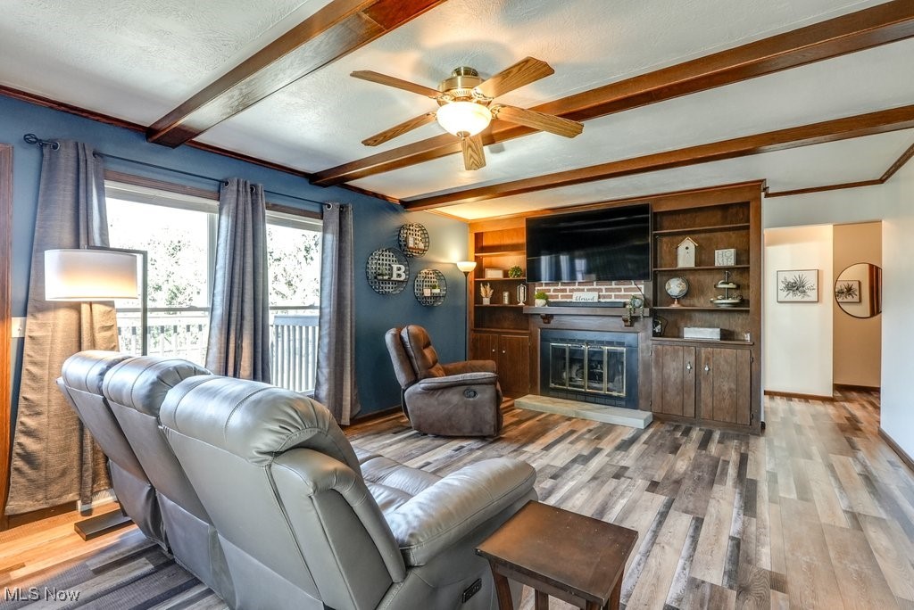 1157 Bass Circle Northwest Canton, OH 44708 - Photo 5 of 31 Living area featuring baseboards, beamed ceiling, wood finished floors, a glass covered fireplace, and a textured ceiling