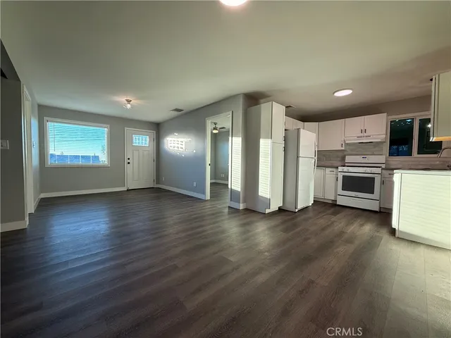 an empty room with wooden floor kitchen view and a window