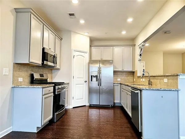 a kitchen with stainless steel appliances granite countertop a stove top oven a sink dishwasher a refrigerator and a microwave oven with wooden floor