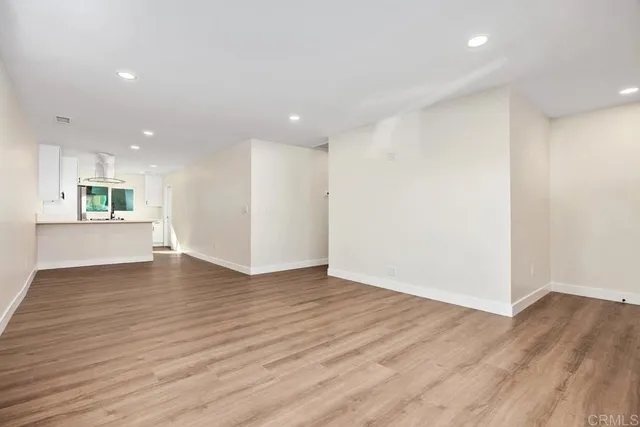 a view of an empty room with wooden floor and a kitchen