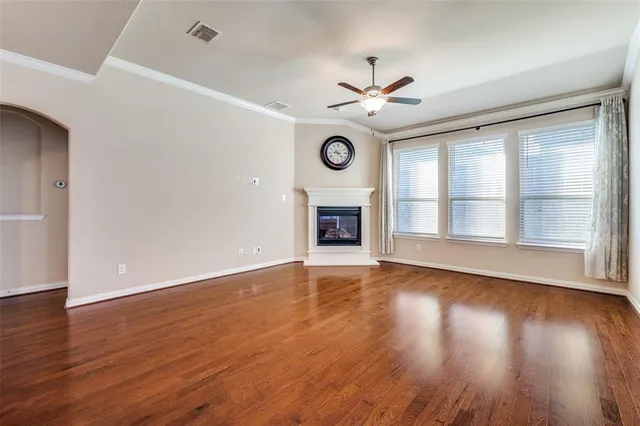 an empty room with wooden floor a ceiling fan a fireplace and windows
