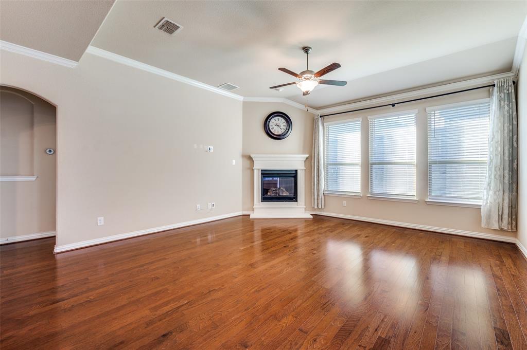16008 Aquilla Way Prosper, TX 75078 - Photo 13 of 33 an empty room with wooden floor a ceiling fan a fireplace and windows