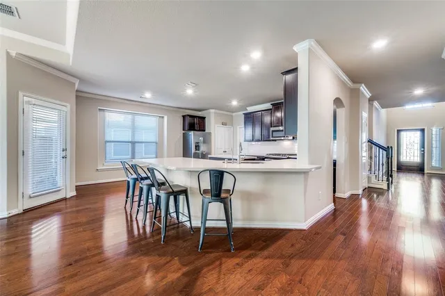 a open kitchen with stainless steel appliances granite countertop a stove a refrigerator a microwave a dining table and chairs with wooden floor