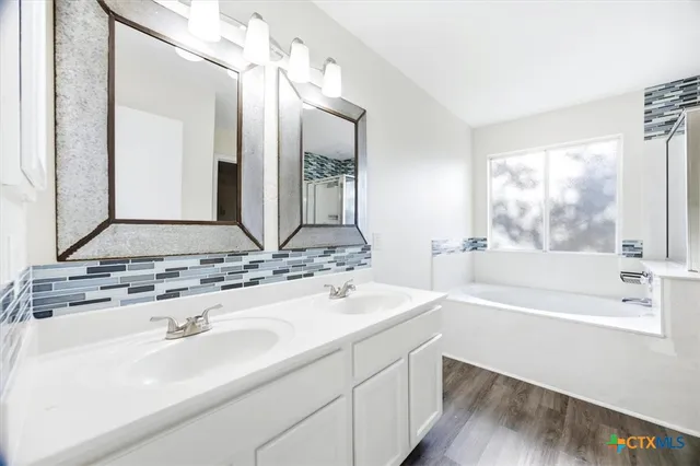 a bathroom with a bathtub a double vanity sink and mirror