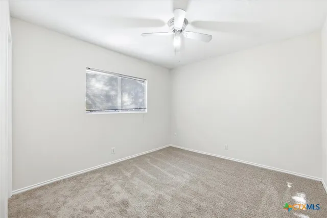 an empty room with a chandelier fan and windows
