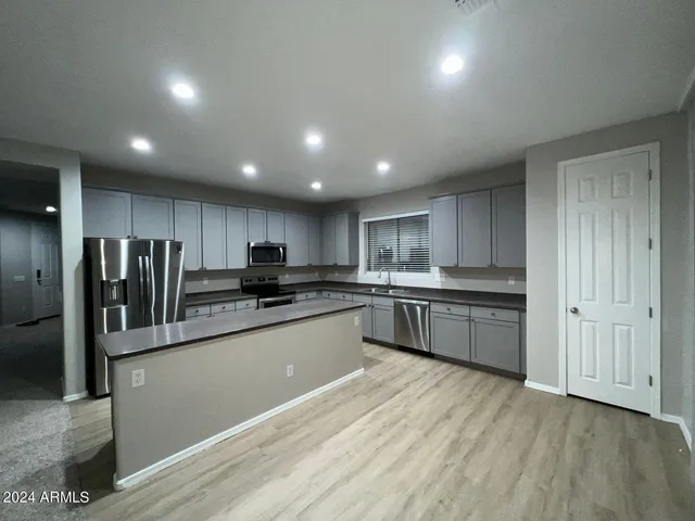 a kitchen with stainless steel appliances kitchen island granite countertop a refrigerator a sink dishwasher and a stove with wooden floor