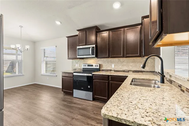 a kitchen with granite countertop wooden cabinets a sink and stainless steel appliances
