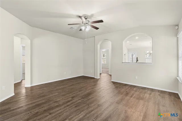 an empty room with wooden floor chandelier fan and windows