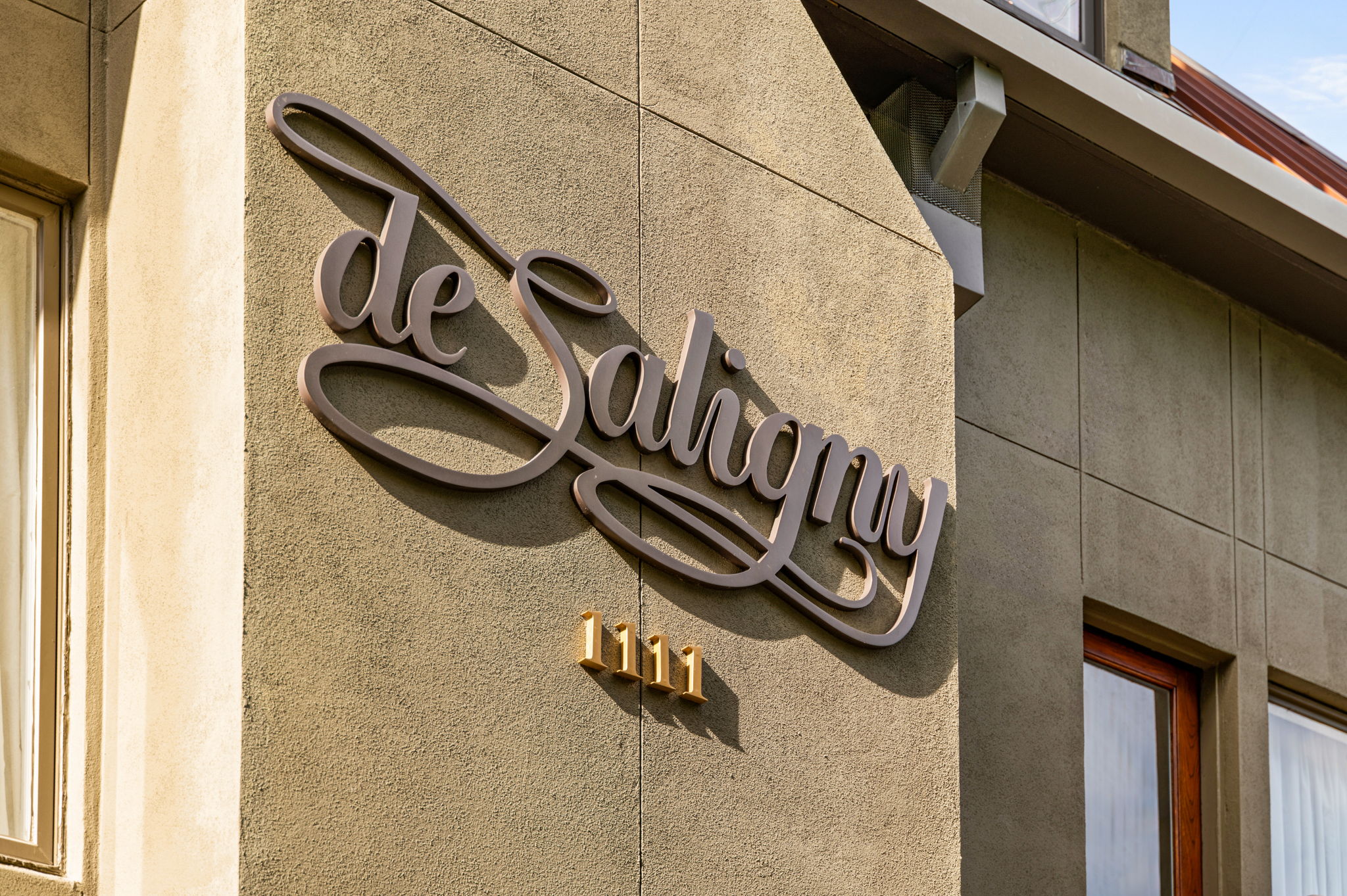 1111 West 12th Street, Unit 107 Austin, TX 78703 - Photo 7 of 38 Stucco exterior with decorative horizontal banding, featuring a large script-style metal sign and prominent brass numerical signage