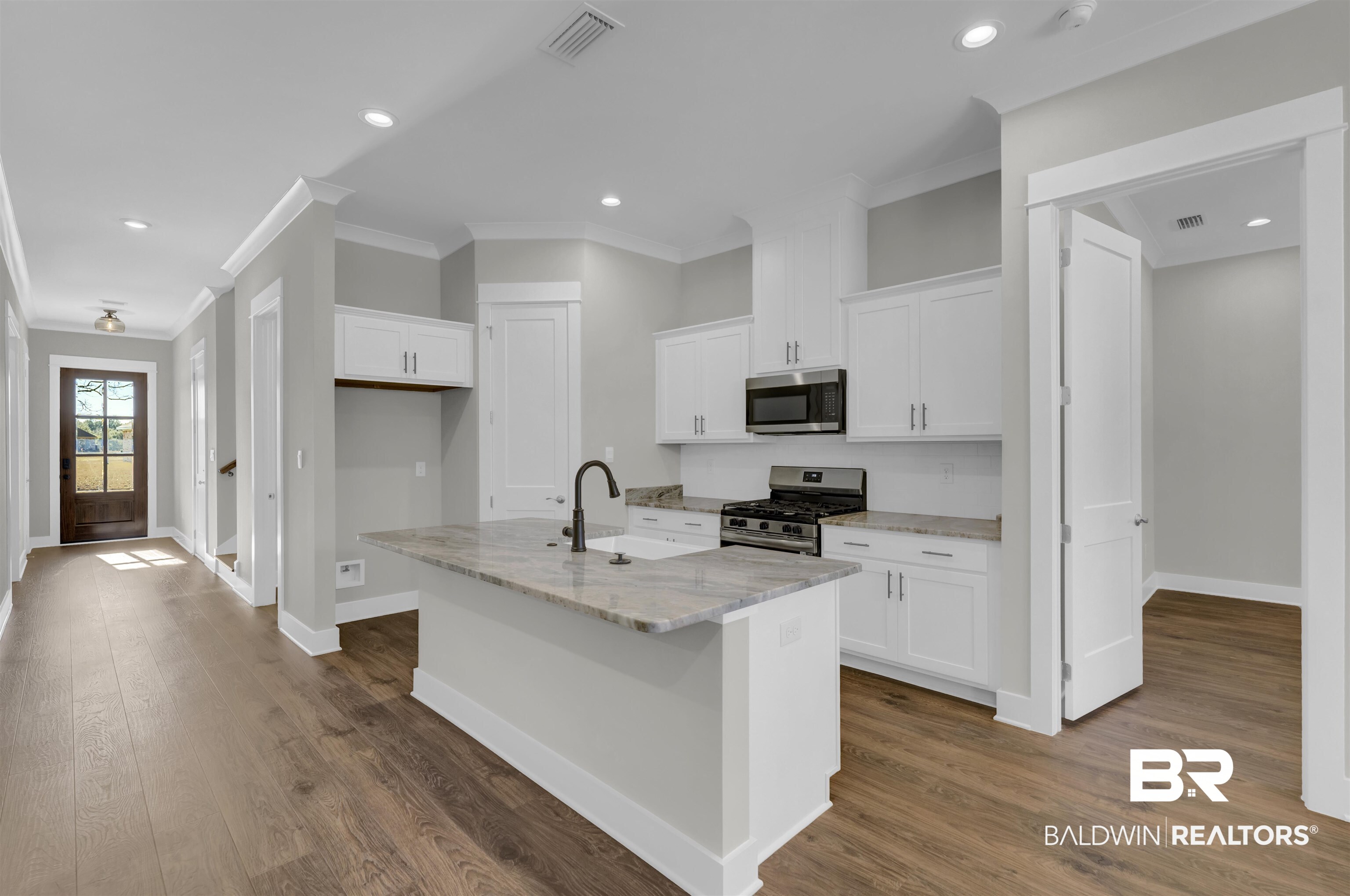571 Morning Mist Way Fairhope, AL 36532 - Photo 5 of 47 Kitchen with white cabinets, light stone counters, stainless steel appliances, crown molding, and an island with sink