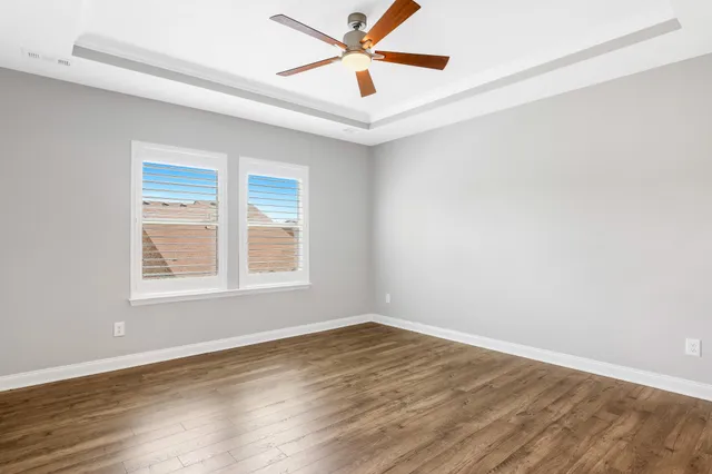 an empty room with wooden floor ceiling fan and windows