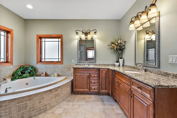 a spacious bathroom with a granite countertop double vanity sink a mirror and a bathtub