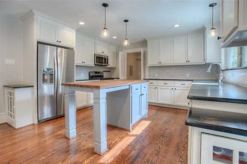 a kitchen with stainless steel appliances granite countertop a refrigerator a sink dishwasher a stove and white cabinets with wooden floor