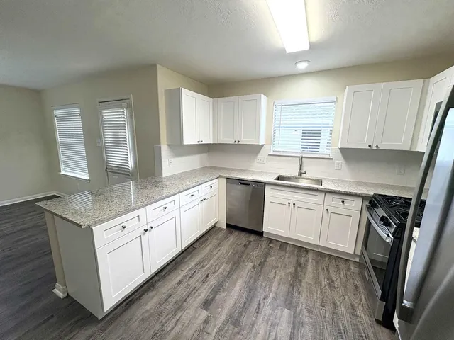 a kitchen with granite countertop a sink cabinets stainless steel appliances and window