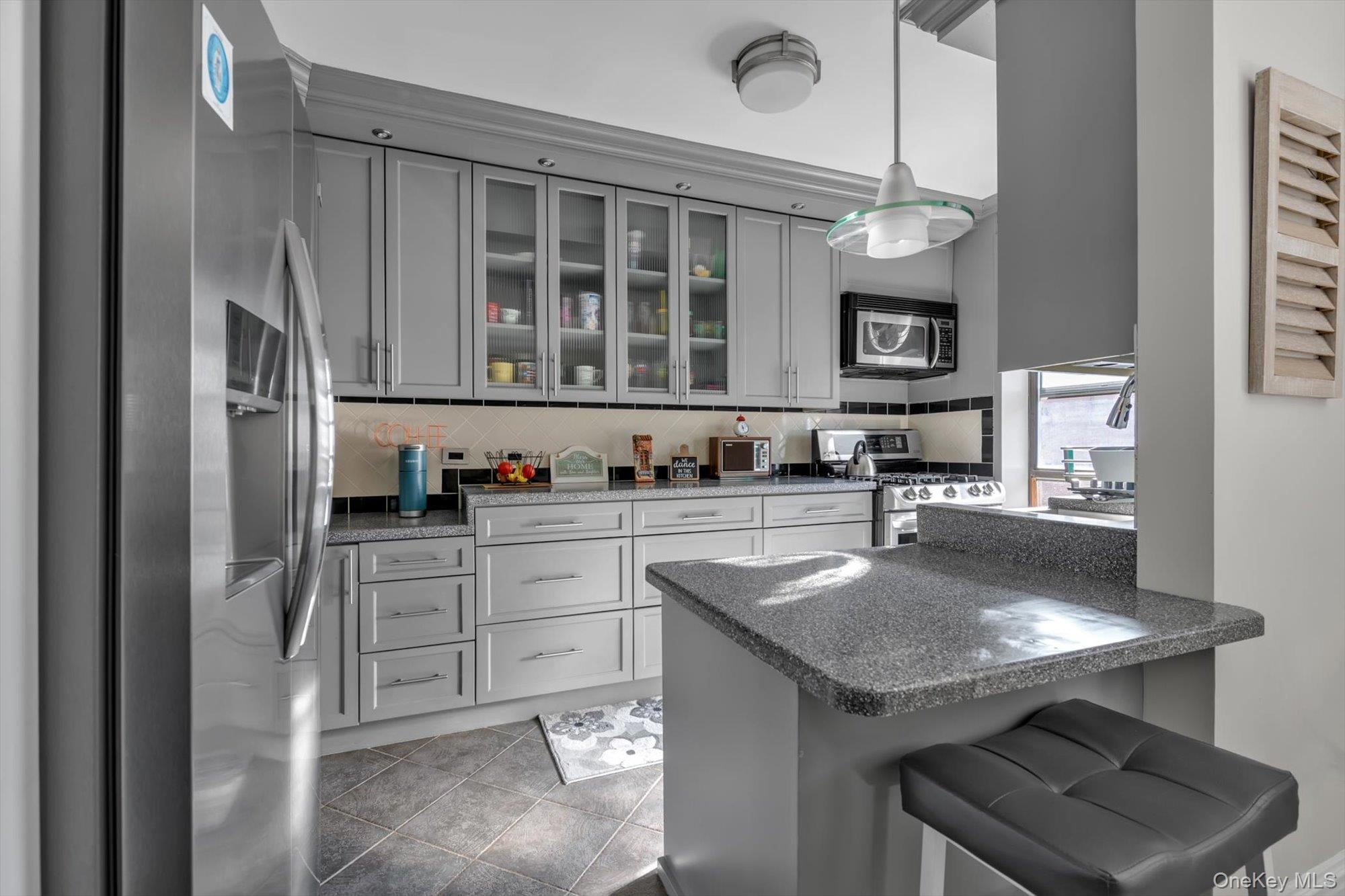 83-25 98th Street, Unit 4L Queens, NY 11421 - Photo 5 of 14 Kitchen with stainless steel appliances, gray cabinets, dark stone counters, a kitchen bar, and decorative light fixtures
