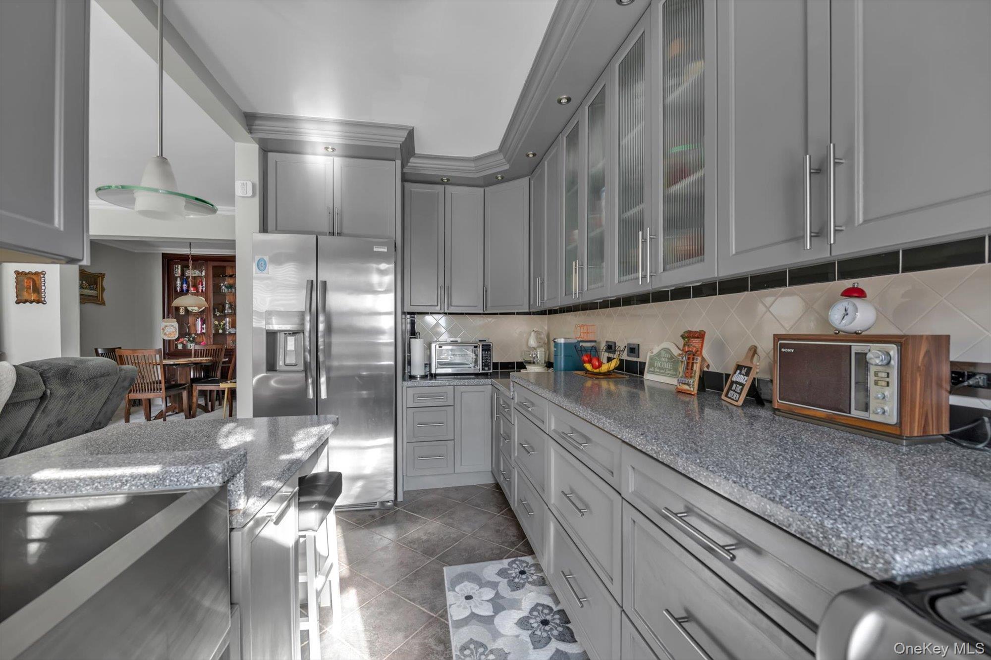83-25 98th Street, Unit 4L Queens, NY 11421 - Photo 7 of 14 Kitchen featuring gray cabinets, stainless steel refrigerator with ice dispenser, glass insert cabinets, dark stone countertops, and decorative backsplash