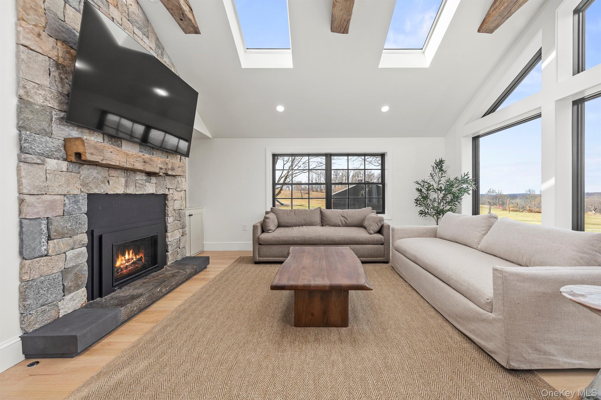 97 Valley Farm Road Millbrook, NY 12545 - Photo 15 of 50 Living room with light wood floors, high vaulted ceiling, a stone fireplace, and a healthy amount of natural light