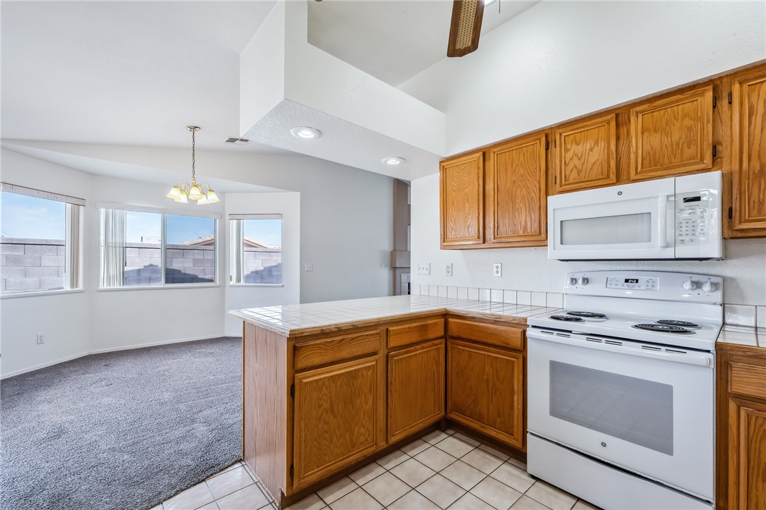 2524 South Ridge Avenue Bullhead City, AZ 86429 - Photo 25 of 64 Kitchen featuring white appliances, a chandelier, a peninsula, brown cabinetry, and vaulted ceiling